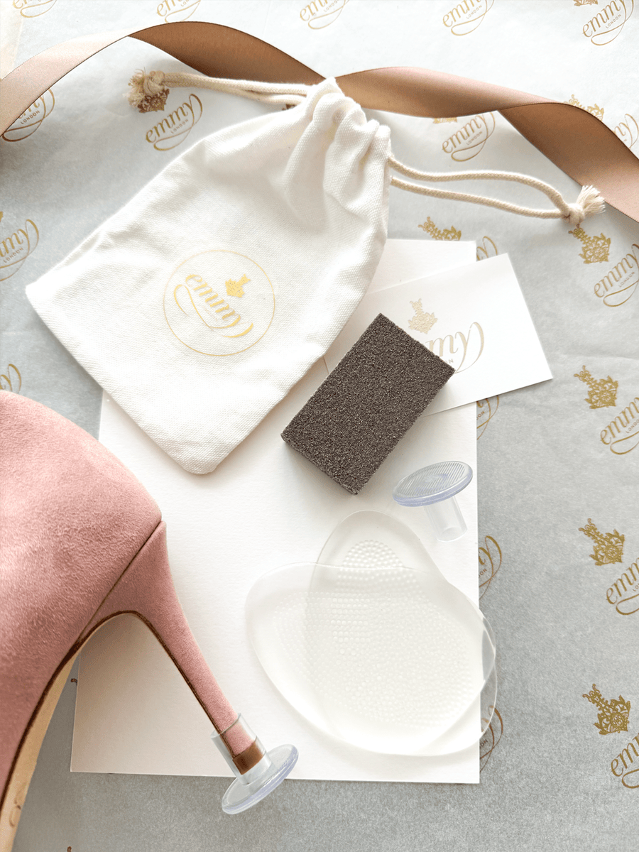 Pink suede heel with a stiletto design, featuring a pointed toe. The heel height is approximately 4 inches. The shoe is positioned on a light background with a branded tissue paper underneath. Accompanying the shoe are a white drawstring pouch, a sponge, and a pair of gel pads, all neatly arranged in the image. image