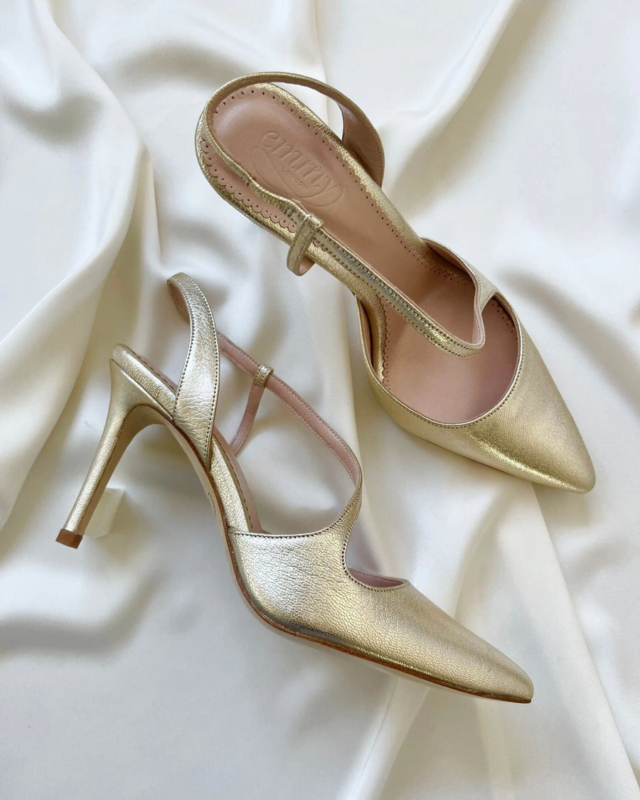Gold slingback heels with a pointed toe design, featuring a delicate strap across the instep. The heels are approximately 3.5 inches high. The shoes are placed on a soft, white fabric background, showcasing their elegant silhouette from a top-down angle. image
