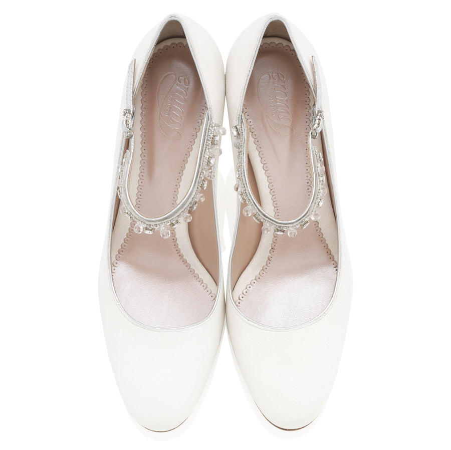 White shoes with a rounded toe and a decorative strap featuring small embellishments across the instep. The shoes are set against a plain white background, showcasing their elegant design from a top-down angle. The heel height is not specified. image