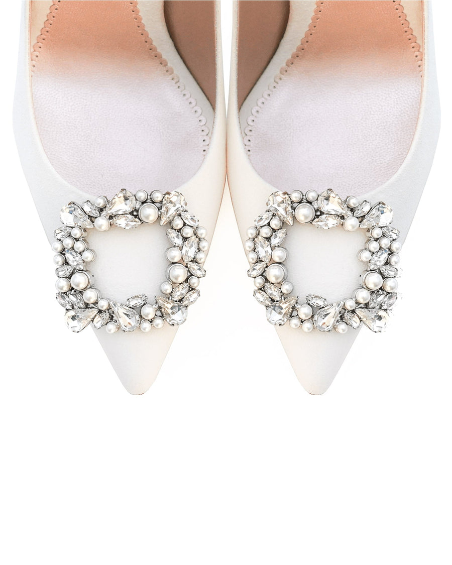 Elegant white pointed-toe heels featuring a decorative crystal and pearl embellishment on the vamp. The shoes are displayed from a top-down angle against a clean white background, highlighting the intricate detailing of the embellishment. image