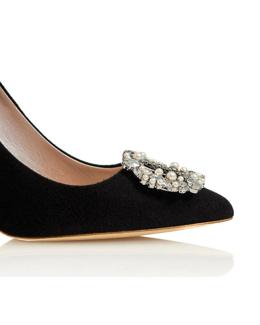 Black suede heels featuring an ornate embellishment on the toe. The image is taken from a close-up angle, highlighting the shoe's elegant design and texture. The background is a clean, white surface, emphasizing the shoe's details. image