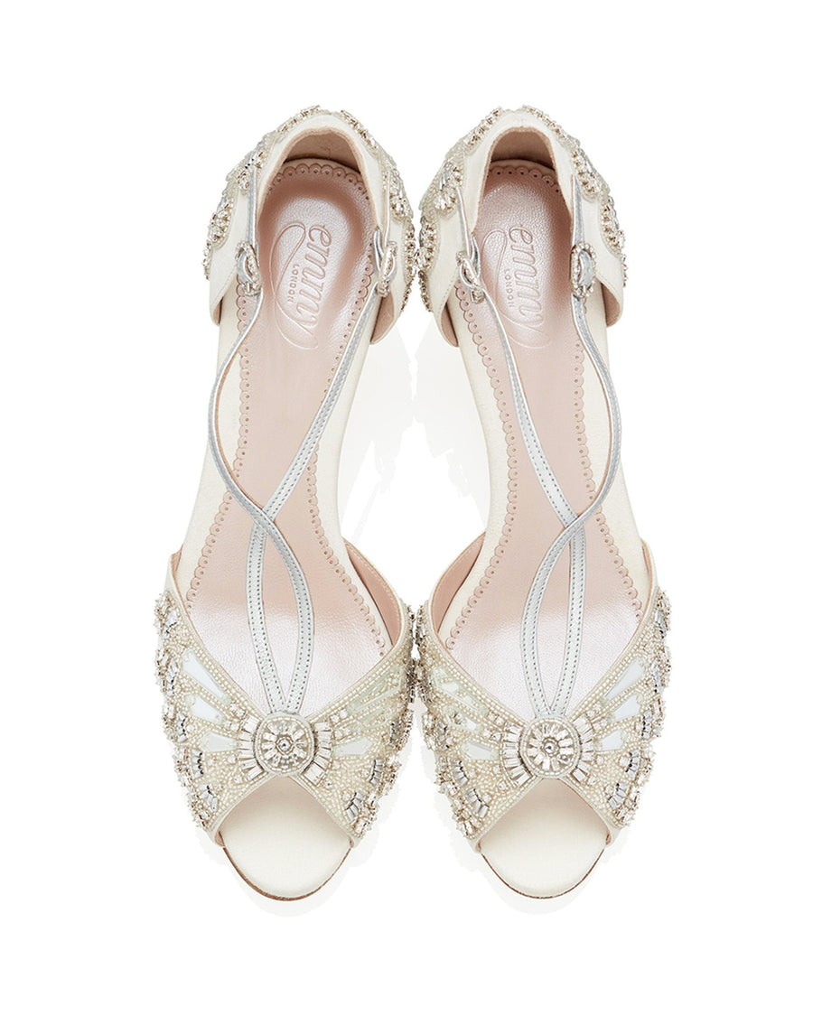 Elegant open-toe heels featuring intricate beading and embellishments on a soft ivory base. The shoes are set against a clean white background, showcasing their delicate design. The angle captures the shoes from above, highlighting the detailed craftsmanship and the elegant straps. image