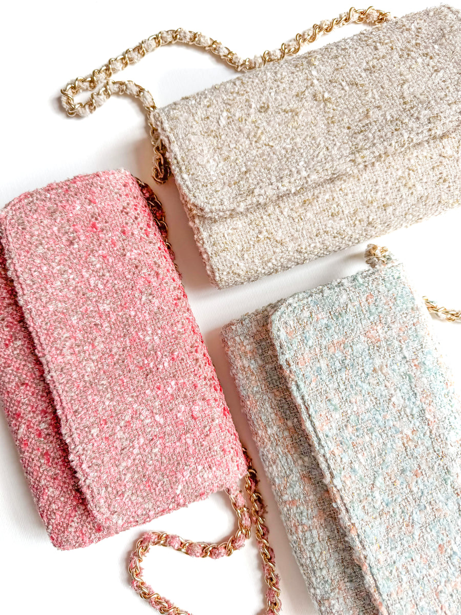 Three stylish tweed clutch bags are displayed on a white background. The bags are in pink, cream, and light blue, each featuring a flap closure and a gold chain strap. The image is taken from a top-down angle, showcasing the texture and colors of the tweed material. image