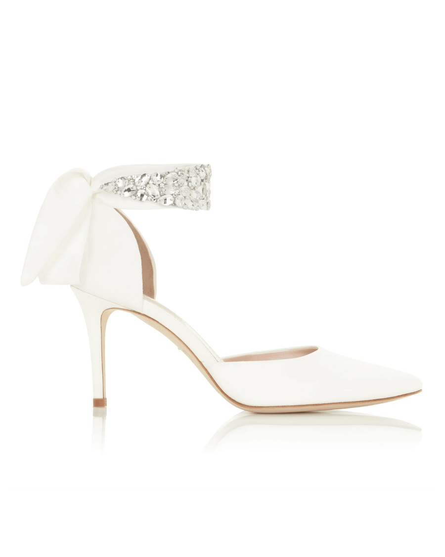 White pointed-toe heels with a delicate ankle strap adorned with sparkling embellishments. The heels are approximately 3.5 inches high, showcasing a sleek silhouette. The background is neutral, emphasizing the elegance of the shoes. The image is taken from a side angle, highlighting the design details. image
