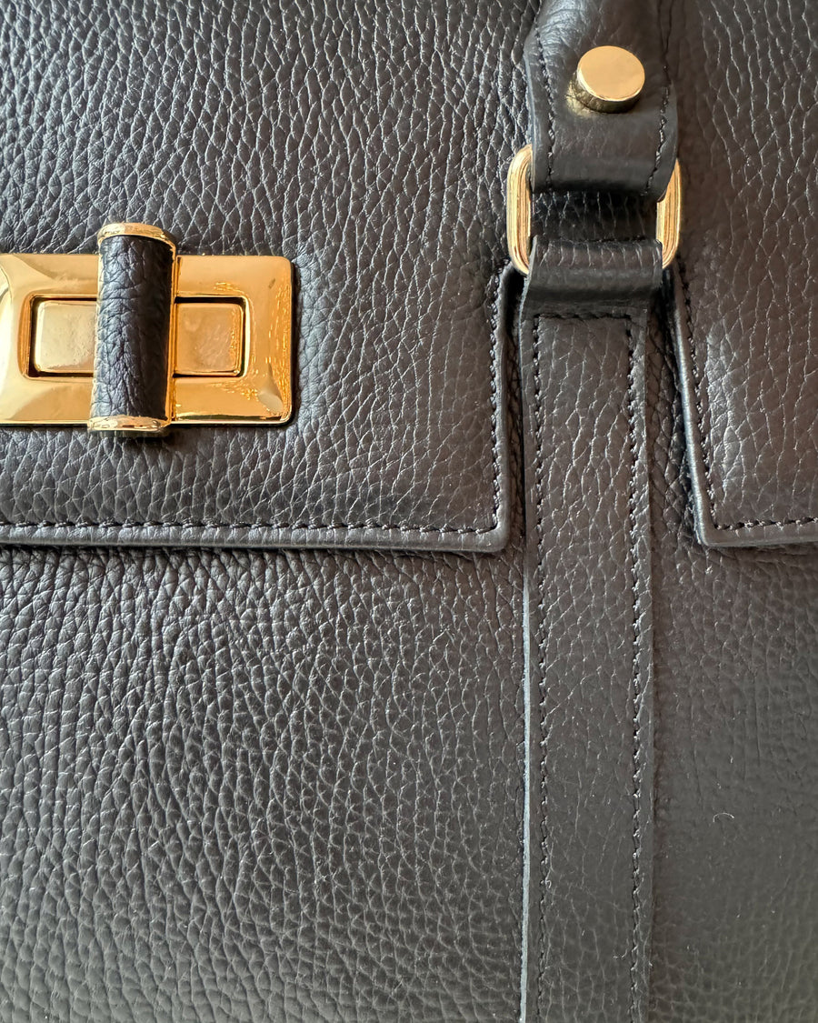 Close-up of a dark gray pebbled leather handbag showing a gold-tone metal clasp and a leather strap detail. image