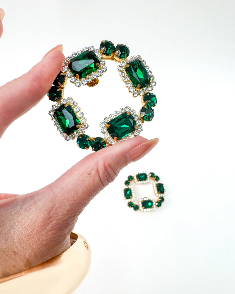 Green crystal shoe clips held by a hand on a white background image