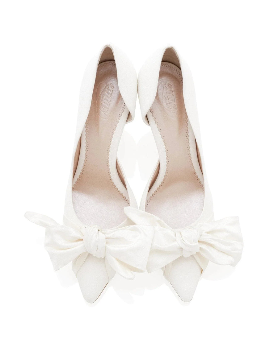 White pointed-toe heels with large fabric bows at the front. The shoes are displayed on a plain white background, showcasing their elegant design. The angle captures the shoes from above, emphasizing the unique bow detail. image