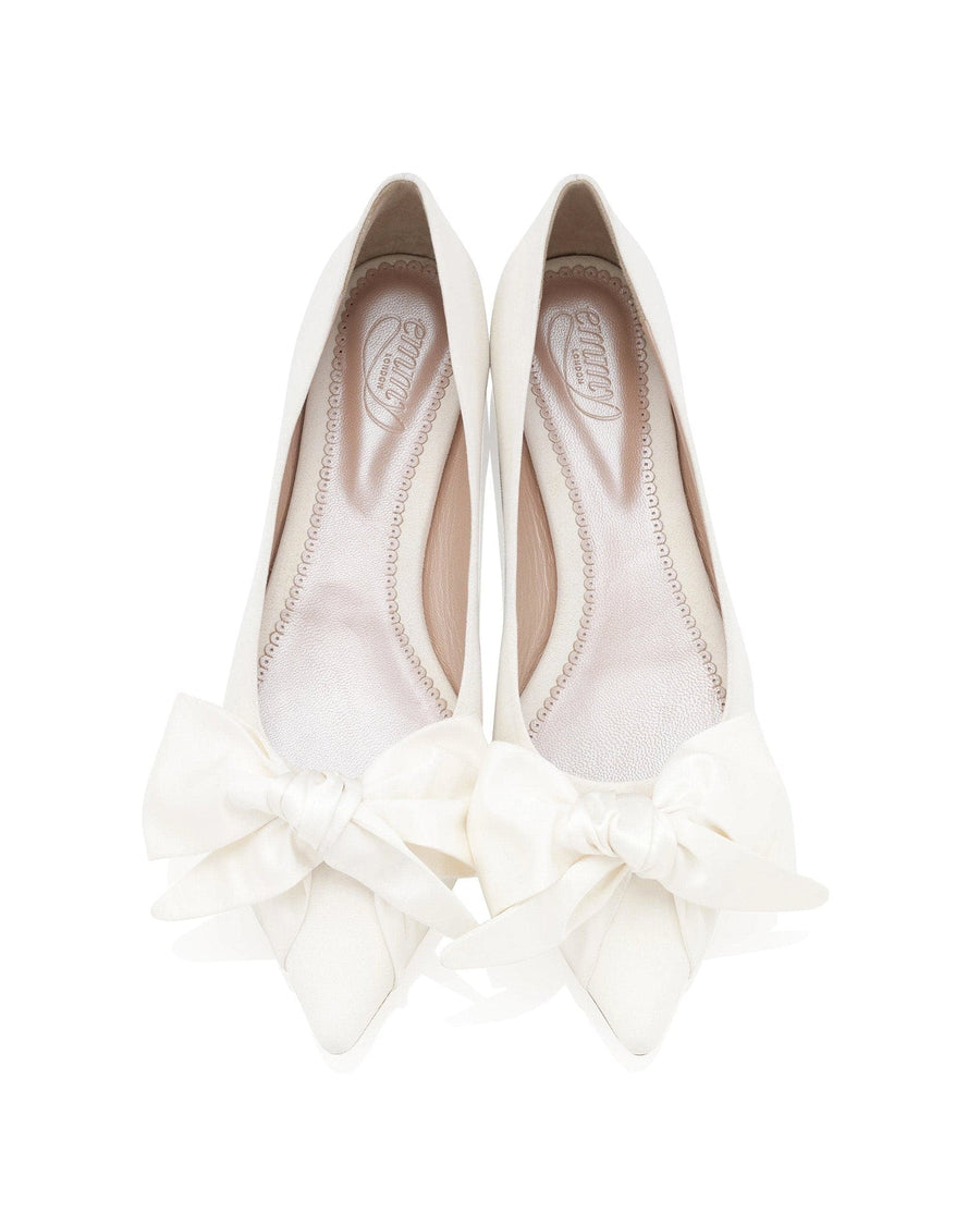 White pointed-toe heels featuring a large bow detail at the front. The shoes are displayed on a plain white background, showcasing their elegant design. The angle captures the shoes from above, highlighting the smooth surface and the intricate stitching along the edges. image