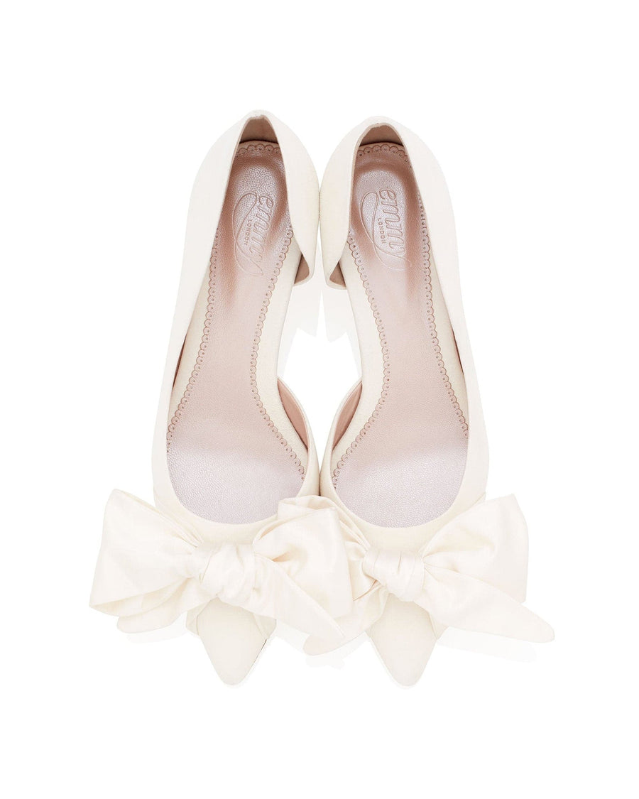 White pointed-toe heels with a large bow detail at the front. The shoes are displayed on a clean, white background, showcasing their elegant design. The angle of the image highlights the smooth finish and the interior lining of the shoes. image