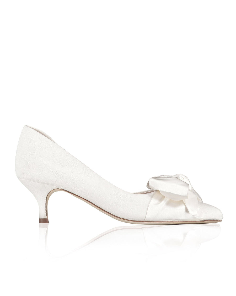 White heels with a delicate bow detail on the toe. The shoes are set against a clean, white background, showcasing their elegant design. The heel height is approximately 2.5 inches, providing a modest lift. image