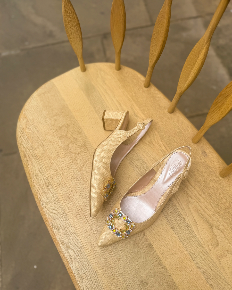 Beige high-heeled shoes with decorative shoe clip on a wooden chair. image