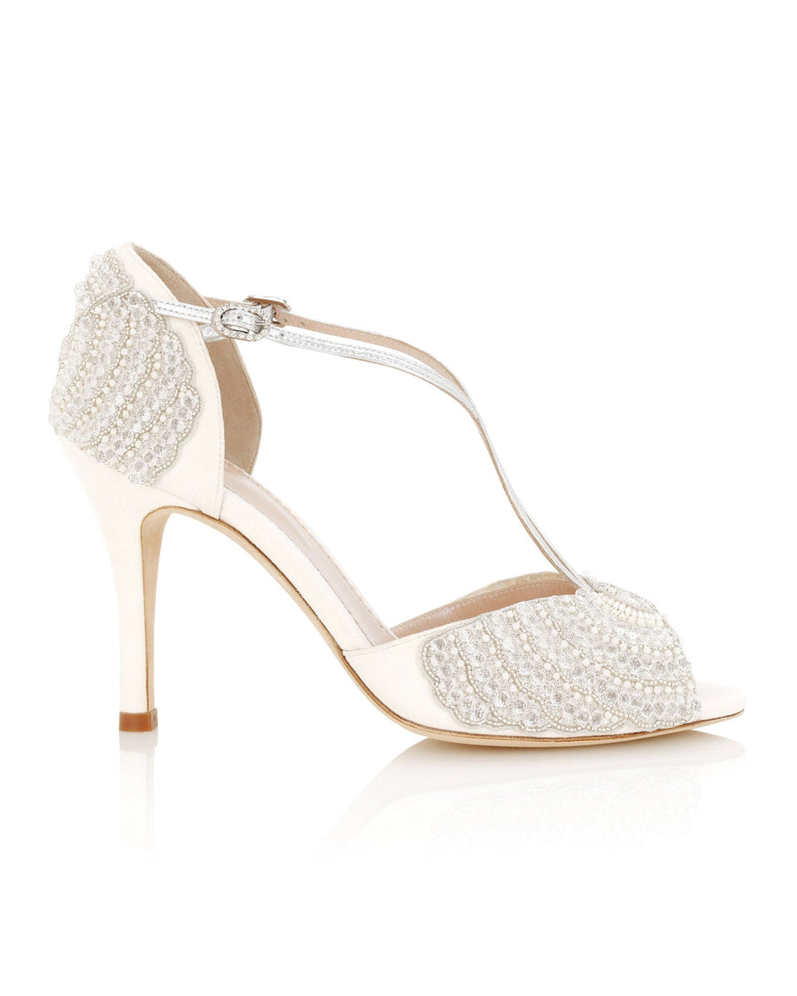 Elegant ivory heels featuring intricate beaded detailing on the back, set against a clean white background. The shoes have a T-strap design and a slender stiletto heel, showcasing a side profile view. image