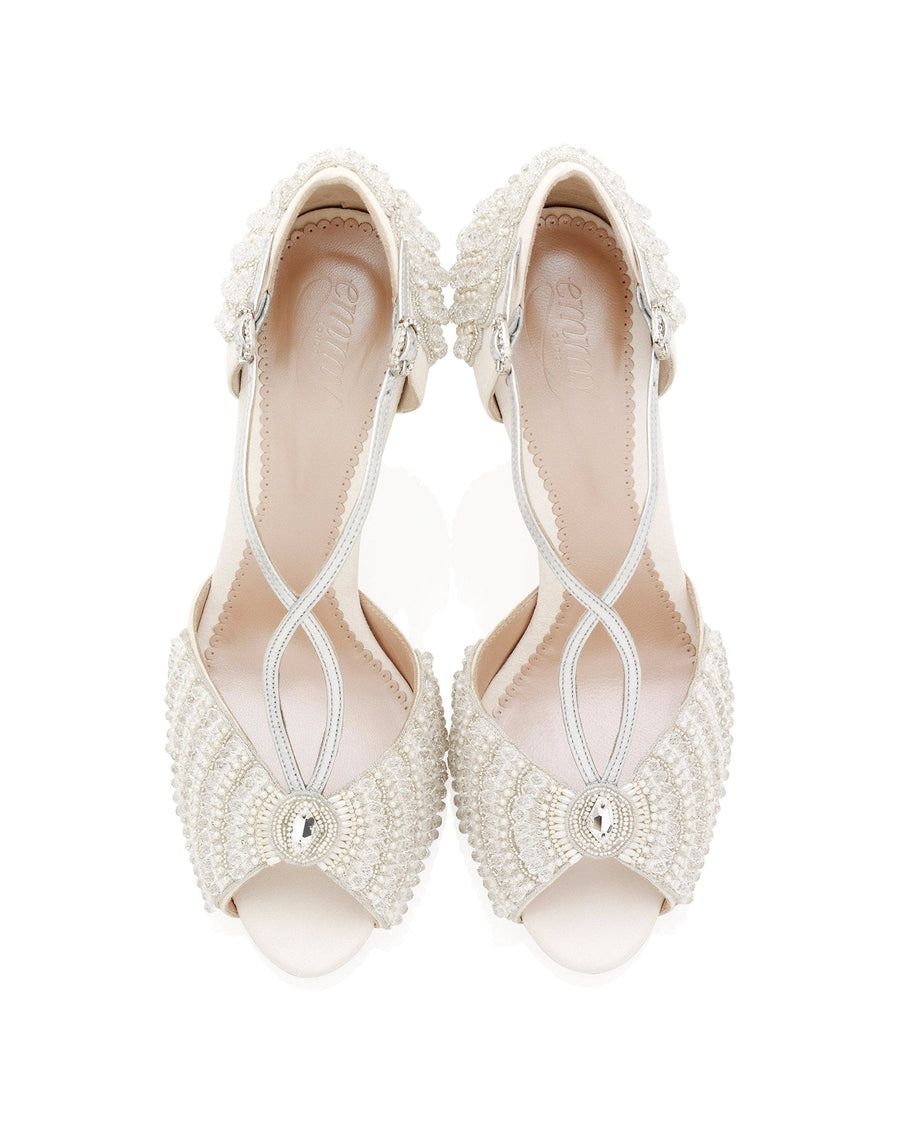 Elegant open-toe heels featuring intricate beading and embellishments in a soft ivory color. The shoes have a delicate crisscross strap design and a slender heel. The image is taken from a top-down angle against a clean white background, showcasing the detailed craftsmanship and luxurious appearance of the footwear. image