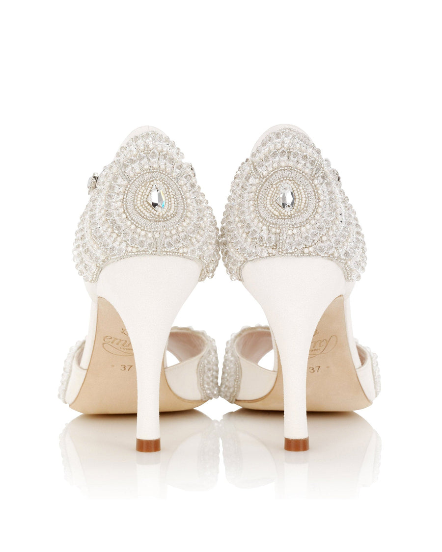 Elegant white heels featuring intricate beading and embellishments on the back. The shoes have a slender stiletto heel and an open-toe design. The image is taken from a straight-on angle, showcasing the detailed craftsmanship. The background is a clean, white surface that highlights the shoes. image