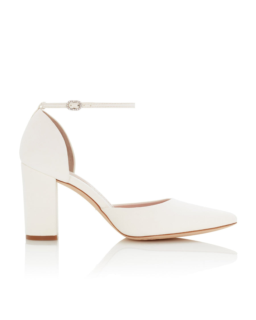 White ankle strap heels with a block heel, featuring a pointed toe design. The shoes are set against a clean, reflective surface, showcasing their elegant silhouette. The heel height is approximately 3.5 inches. The material is likely leather, providing a sleek and polished look. image