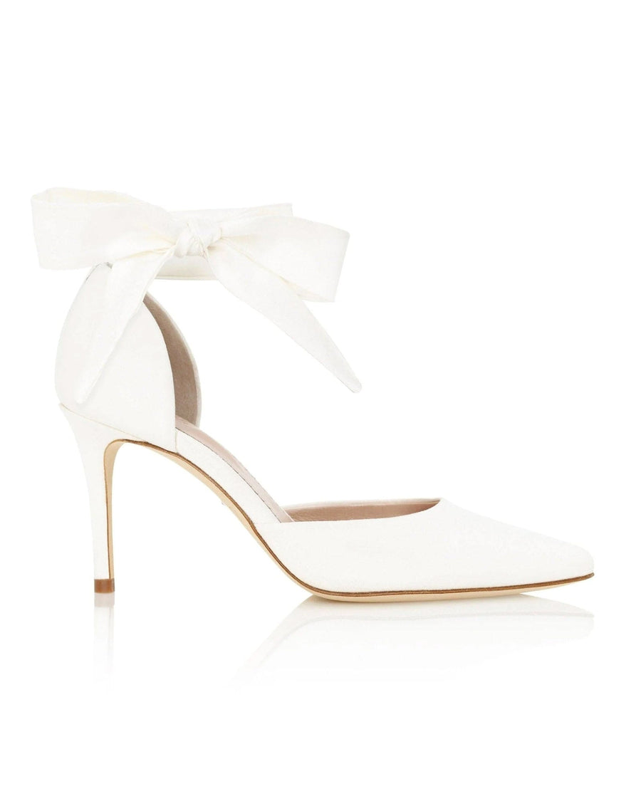 White pointed-toe heels with a delicate ankle strap featuring a bow detail. The shoes are set against a clean, white background, showcasing their elegant design. The heel height is approximately 3.5 inches, and the material is leather. image