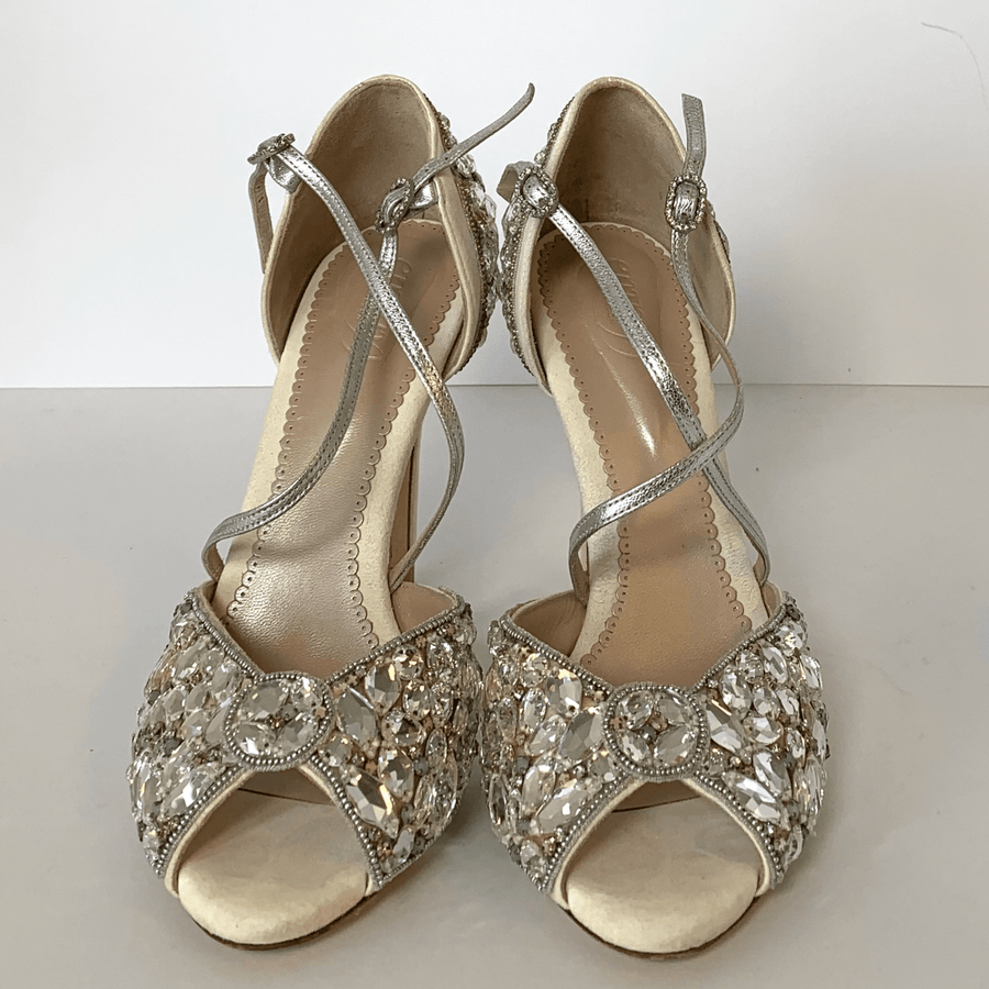 Elegant open-toe heels featuring a sparkling embellished design on the front, set against a clean white background. The shoes have delicate silver straps that wrap around the ankle, showcasing a mid-height heel. image