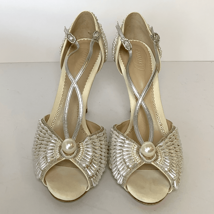 Elegant silver heels featuring intricate beading and a pearl accent at the front. The shoes have a delicate crisscross strap design and a modest heel. The image is taken from a top-down angle against a plain white background, showcasing the detailed embellishments and overall design. image