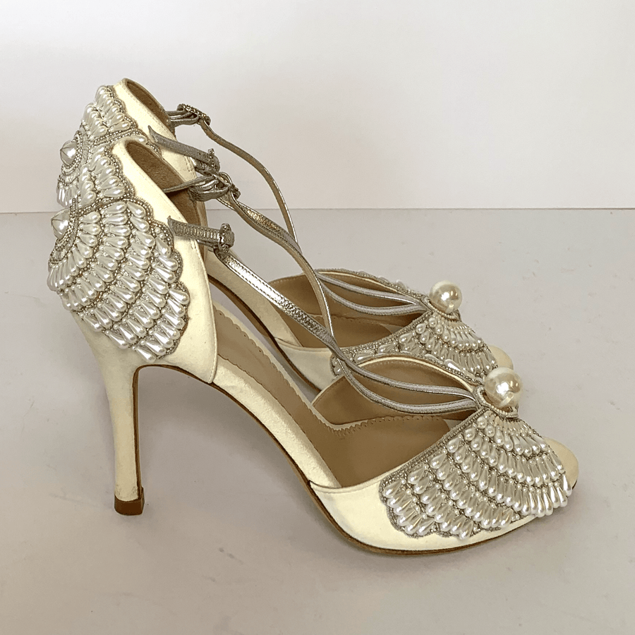 Elegant high-heeled shoes featuring a delicate pearl embellishment and intricate shell-like design on the front. The shoes are set against a plain white background, showcasing their detailed craftsmanship. The heels are approximately 4 inches tall, providing a sophisticated lift. The straps are silver, adding a touch of glamour to the overall look. image