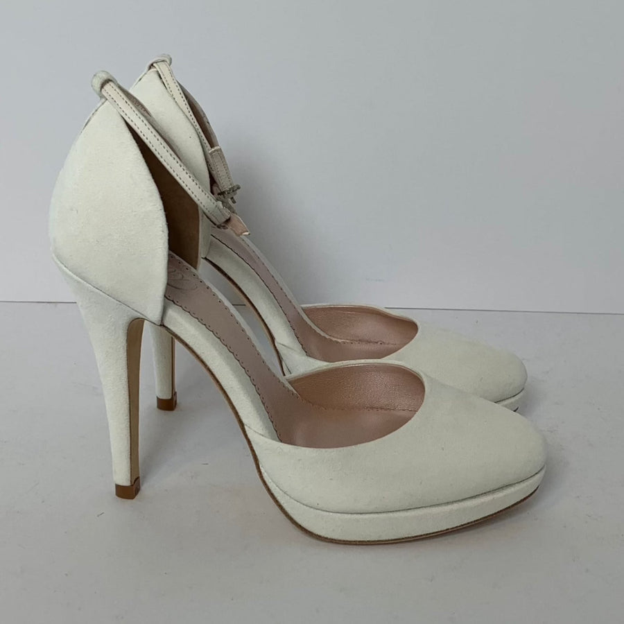 White suede high heels with a sleek design, featuring a rounded toe and a delicate ankle strap. The heels are approximately 4 inches tall. The shoes are displayed on a plain white background, showcasing their elegant silhouette from a side angle. image