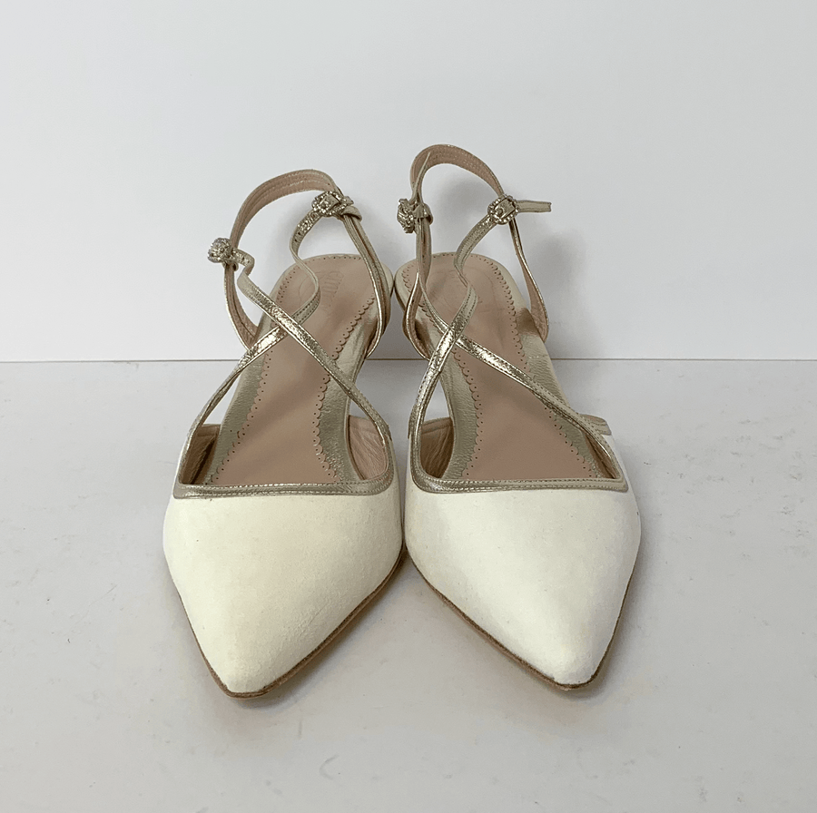 White suede pointed-toe heels with a low heel, featuring delicate gold straps. The shoes are displayed against a plain white background, showcasing their elegant design from a top-down angle. image