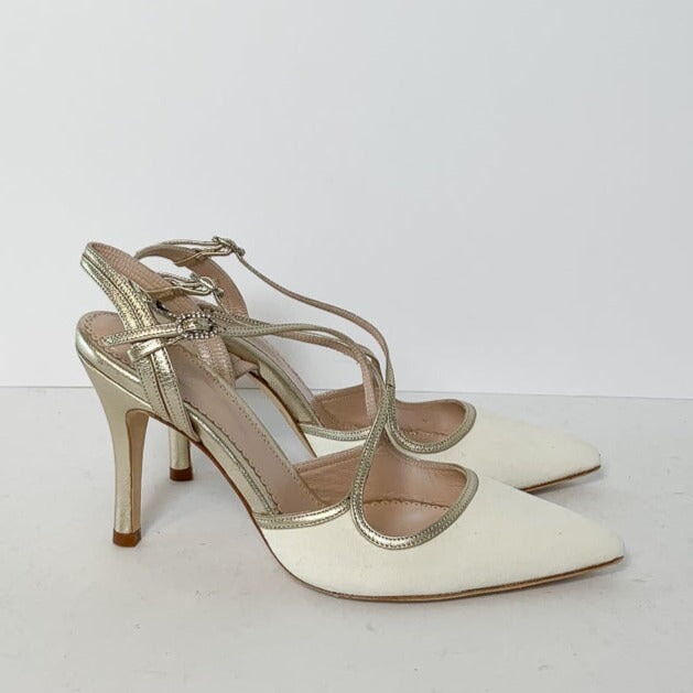 White pointed-toe heels with a gold strap detail, featuring a mid-height heel. The shoes are displayed on a plain white background, showcasing their elegant design. image