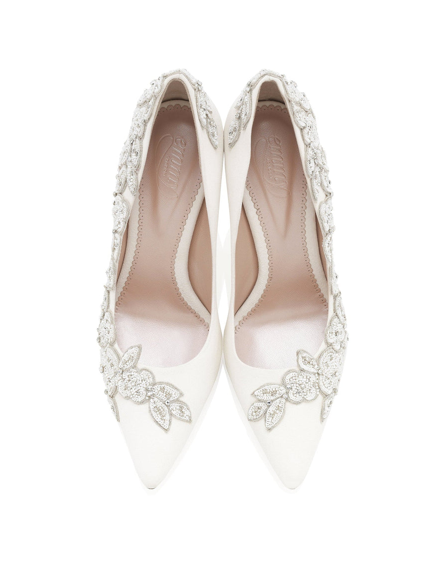 Elegant white heels adorned with intricate floral embellishments and sparkling details. The shoes feature a pointed toe design and a sleek silhouette. The image is taken from a top-down angle, showcasing the delicate craftsmanship. The background is plain, emphasizing the shoes' luxurious appearance. image