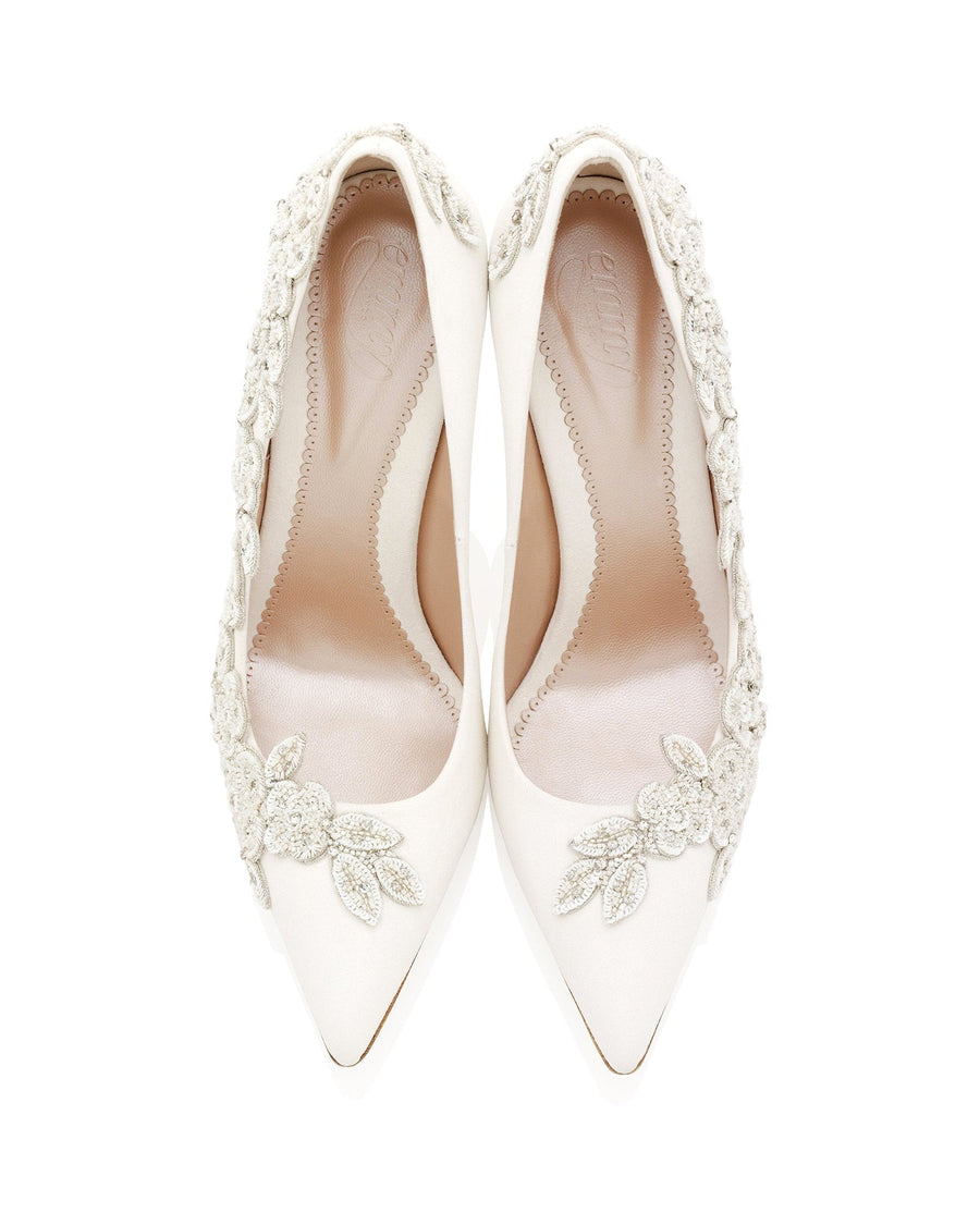 Elegant white heels adorned with intricate floral embellishments, set against a clean white background. The shoes feature a pointed toe design and a sleek silhouette, showcasing a luxurious finish. image