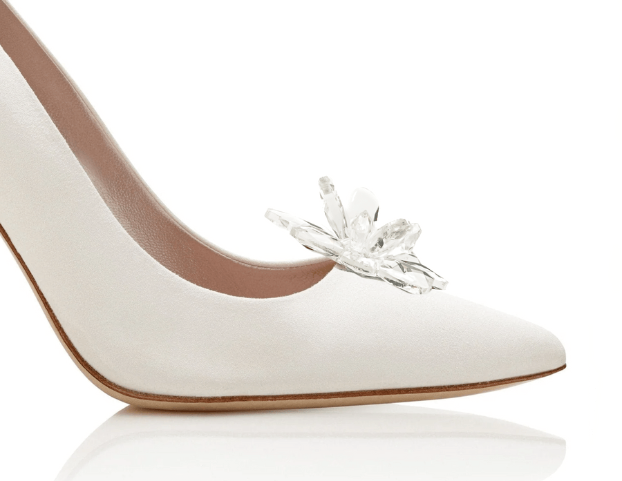 Elegant white leather heels featuring a pointed toe and a decorative crystal embellishment on the front. The image showcases the shoe from a side angle against a clean, white background, highlighting the sleek design and the delicate details of the embellishment. image