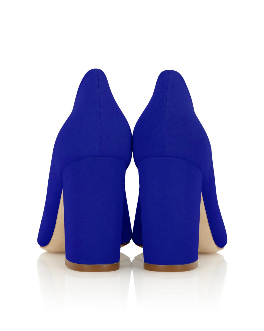 Blue suede heels with a chunky block heel, viewed from the back. The background is plain white, highlighting the shoe's vibrant color and smooth texture. The heel height is approximately 3 inches. image