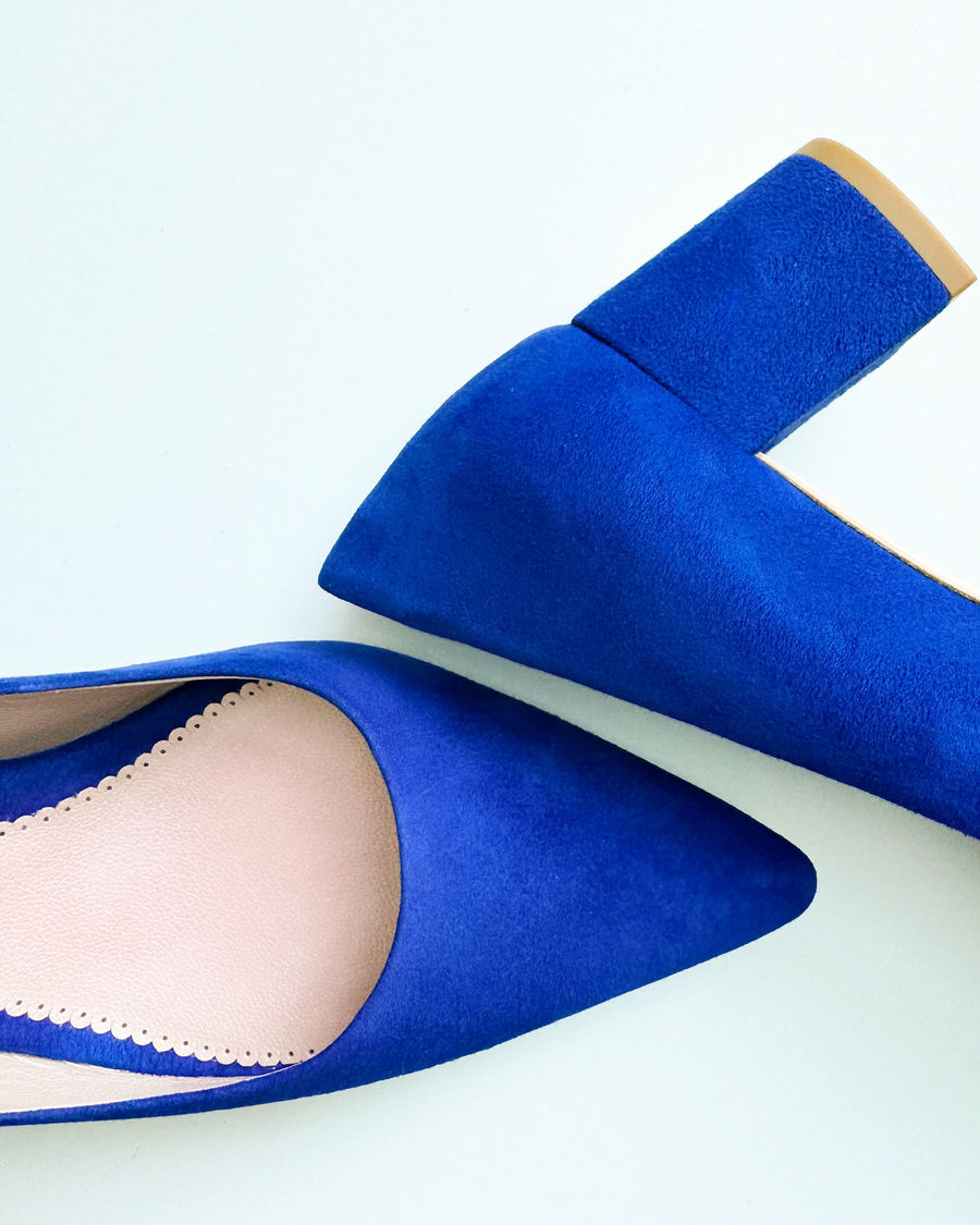 Blue suede heels with a pointed toe design and a chunky heel. The image is taken from a top-down angle, showcasing the texture of the suede. The background is a light, neutral color, emphasizing the vibrant blue of the shoes. image