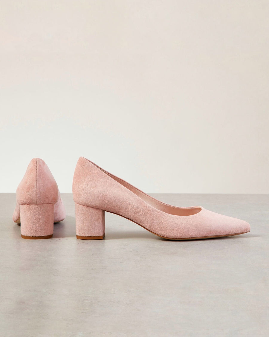 Pink suede block-heeled shoes are displayed against a neutral background. The shoes feature a pointed toe and a chunky heel, providing a stylish yet comfortable look. The image captures the shoes from both the side and back angles, showcasing their elegant design. image