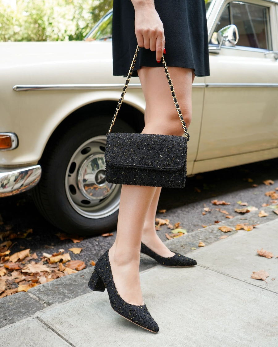 Person wearing black shoes and holding a black clutch in front of a vintage car. image
