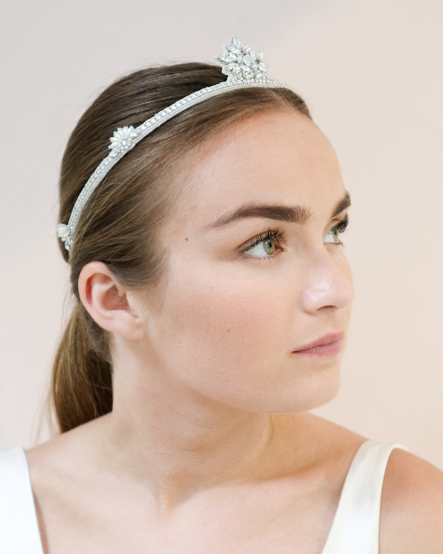 A young woman is wearing a sparkling tiara adorned with intricate floral designs. The tiara is set against a soft, neutral background, highlighting its elegance. The woman has a serene expression, and her hair is styled neatly, complementing the tiara beautifully. image