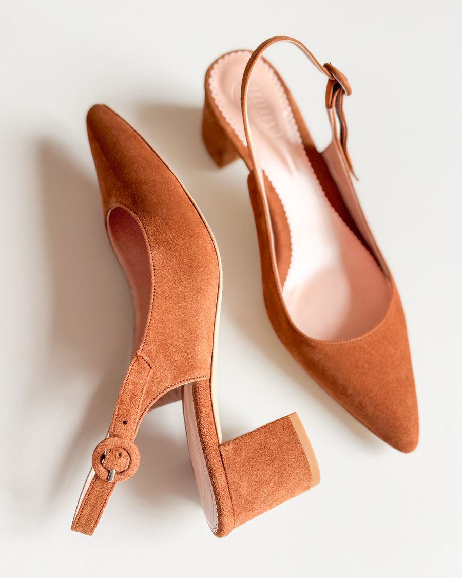 Brown suede slingback heels with a block heel, positioned on a light background. The shoes feature a pointed toe and a decorative buckle on the strap. The image captures the shoes from a top-down angle, showcasing their elegant design. image