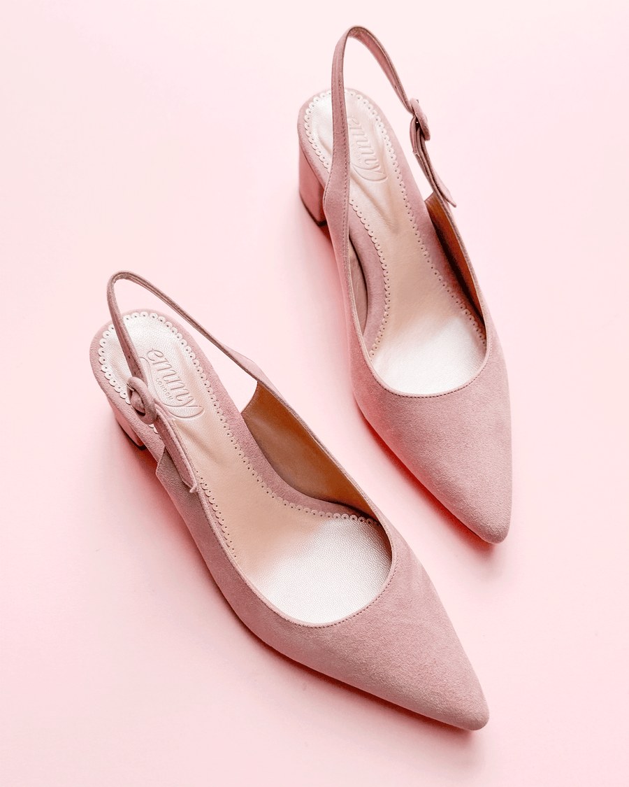 Slingback shoes in soft pink suede with a pointed toe and a modest block heel. The shoes are positioned on a light pink background, showcasing their elegant design. The angle highlights the open back and the adjustable strap, emphasizing their stylish and comfortable fit. image