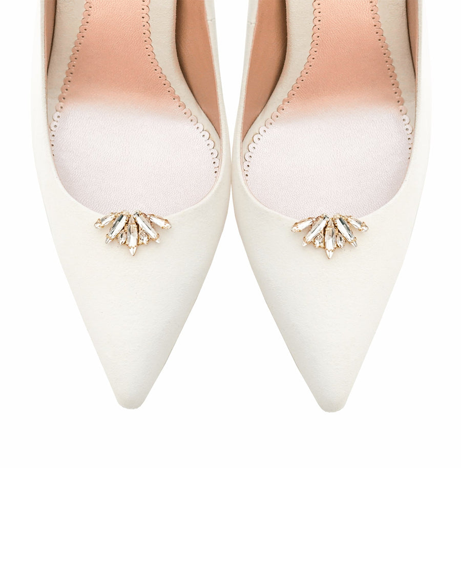 Elegant white pointed-toe heels featuring a decorative crystal embellishment at the front. The shoes are displayed from a top-down angle against a plain white background, highlighting their sleek design and smooth finish. image