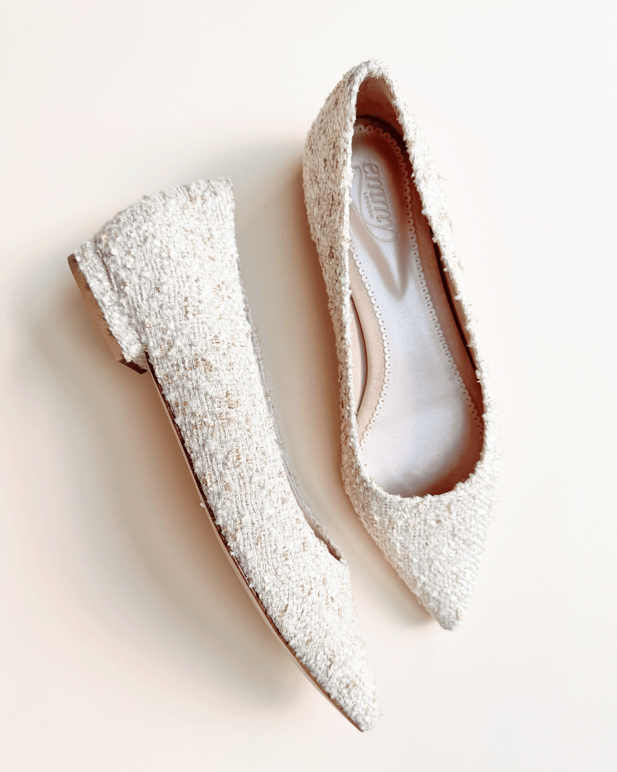 Pointed-toe flats made of tweed, featuring a textured white surface. The shoes are displayed on a light background, showcasing their elegant design. The angle captures both shoes side by side, emphasizing their sleek silhouette. image