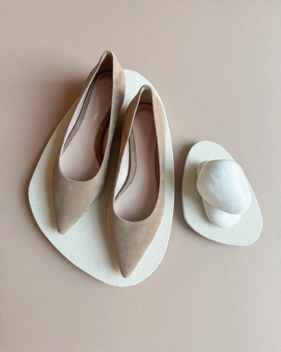 Pointed-toe flats made of suede, displayed on a soft beige background. The shoes are positioned neatly, showcasing their elegant design. No heel height is specified. image