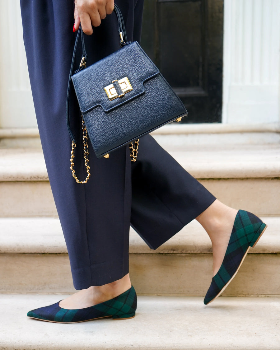 Person holding a navy handbag with gold chain detail, wearing navy pants and green shoes on steps. image