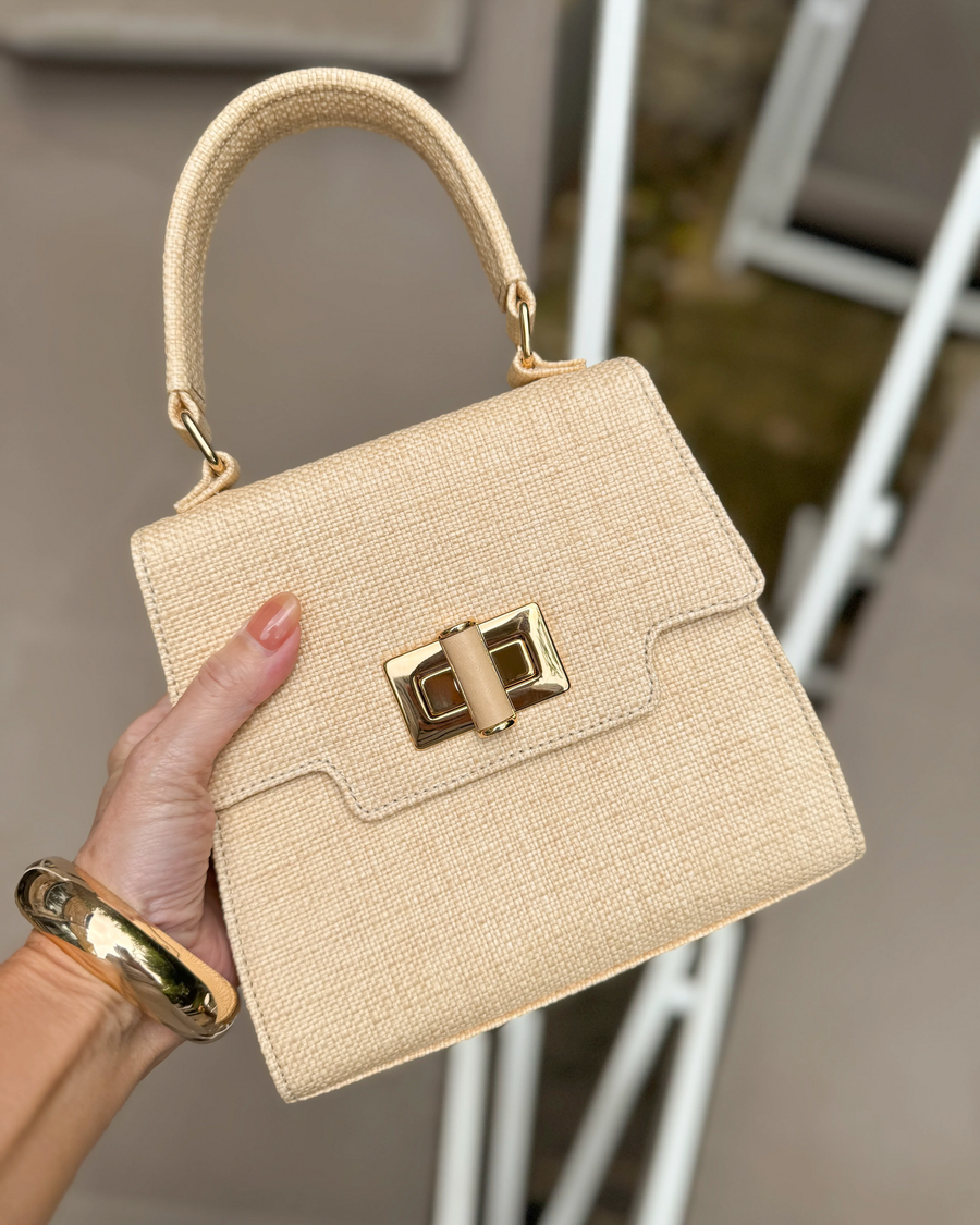Beige handbag with gold accents held by a hand against a neutral background image
