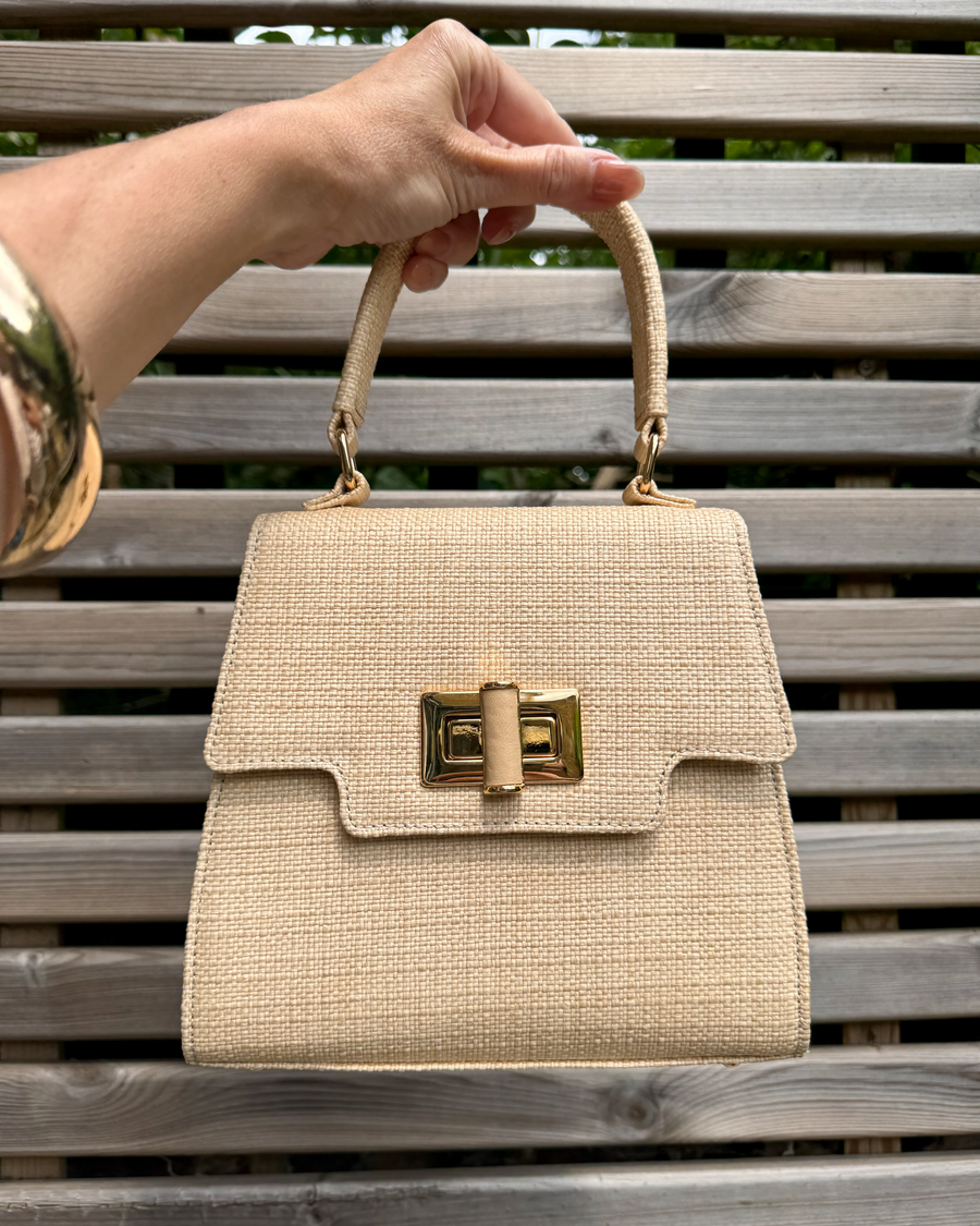 Beige handbag with gold accents held by a hand on a wooden bench image
