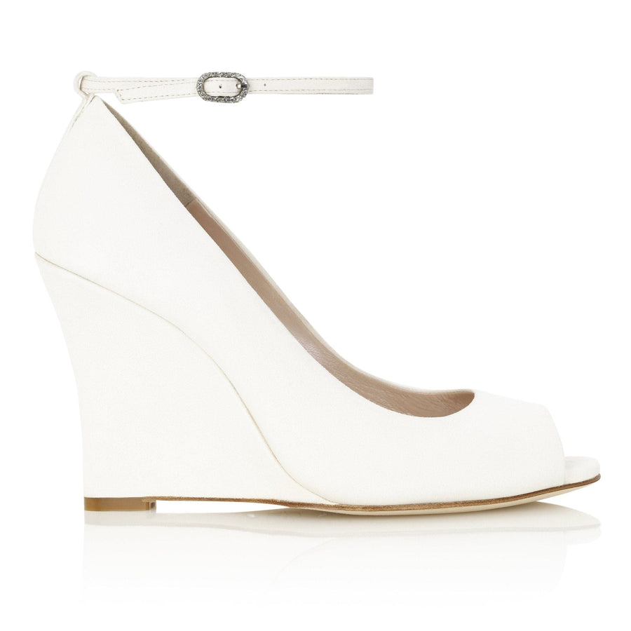 White wedge heels with a peep-toe design and an ankle strap featuring a decorative buckle. The shoes are made of leather and have a high wedge heel. The image is taken from a side angle against a plain white background, showcasing the sleek silhouette of the shoe. image