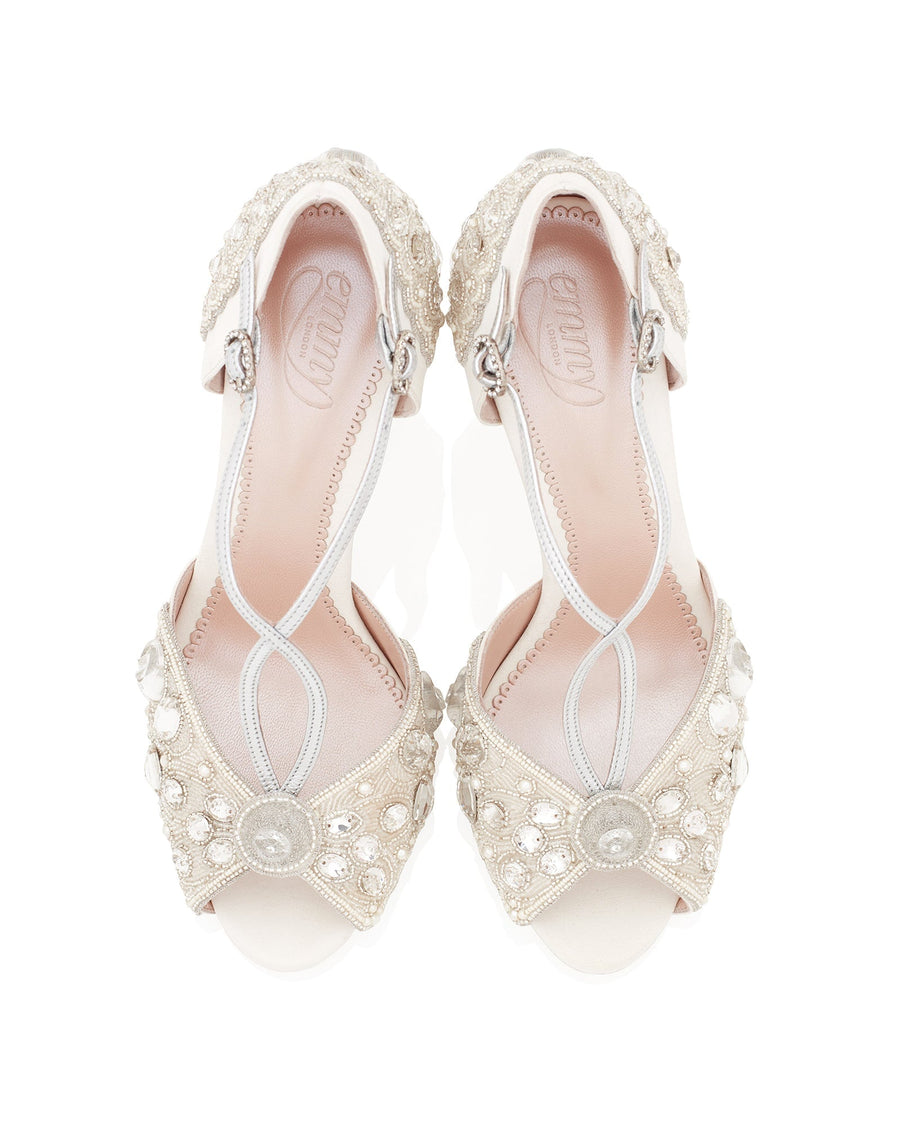 Elegant ivory heels adorned with intricate beading and embellishments. The shoes feature a delicate crisscross strap design and a peep-toe style. The image is taken from a top-down angle against a white background, showcasing the detailed craftsmanship and luxurious appearance of the footwear. image