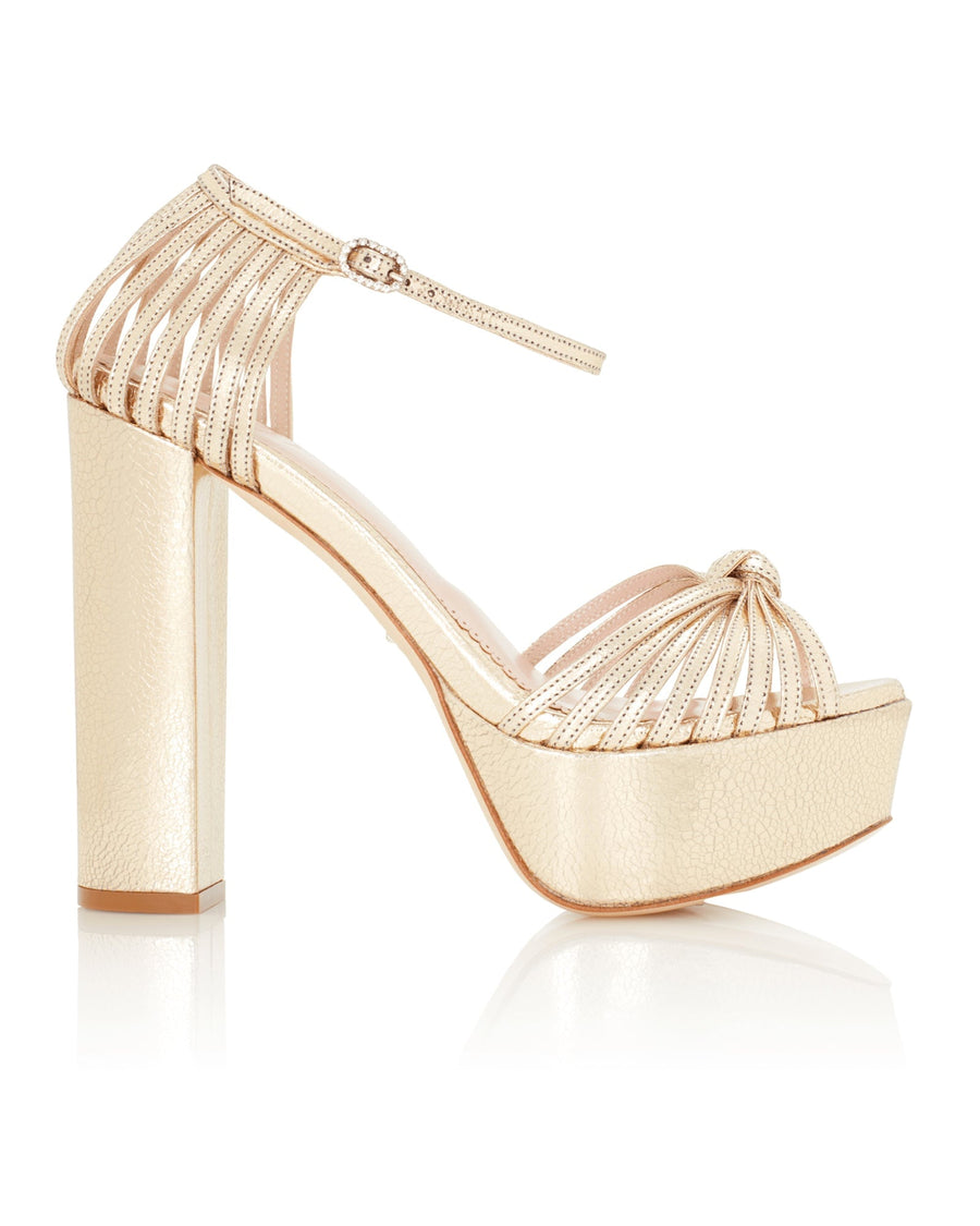 Strappy platform heels in a metallic nude finish, featuring a high block heel and a rounded toe. The design includes vertical cutouts and a delicate ankle strap. The shoes are displayed against a white background, showcasing their elegant silhouette from a side angle. image