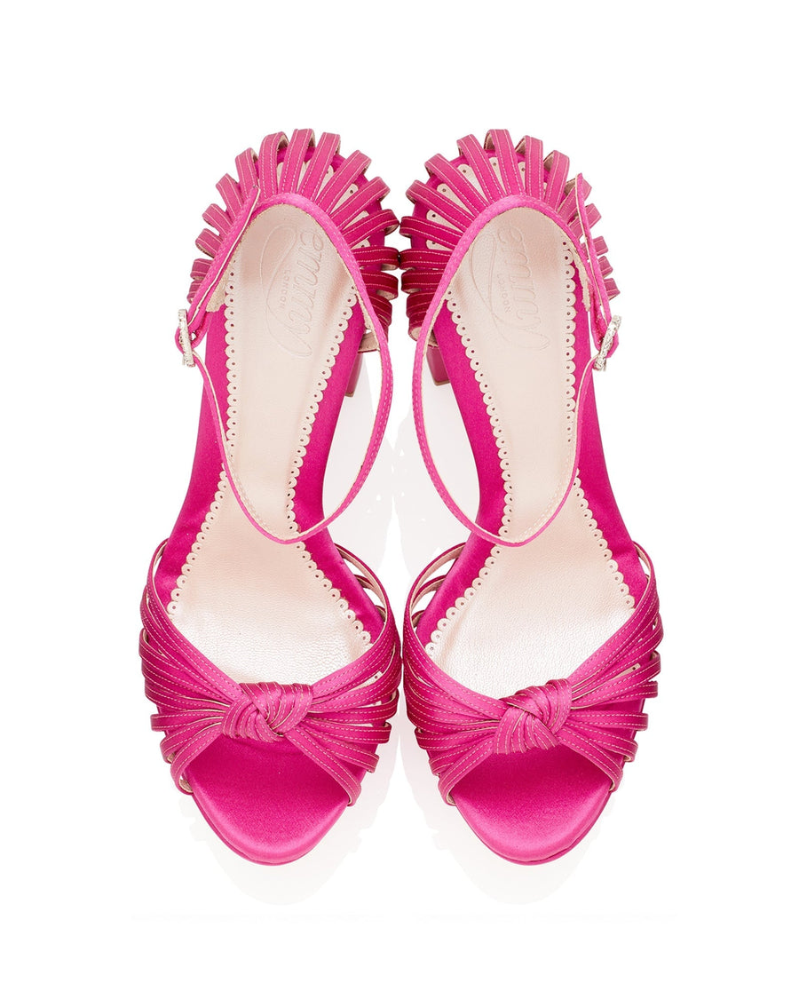Pink heels with a decorative fringe detail at the toe and an elegant knot design. The shoes feature an open toe and a slingback strap. The image is taken from a top-down angle against a white background, showcasing the vibrant color and intricate design. image