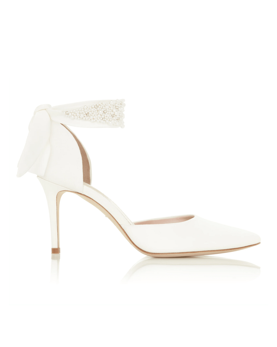 White pointed-toe heels with a delicate ankle strap featuring beaded detailing. The shoes are set against a neutral background, showcasing their elegant design from a side angle. The heel height is approximately 4 inches. image
