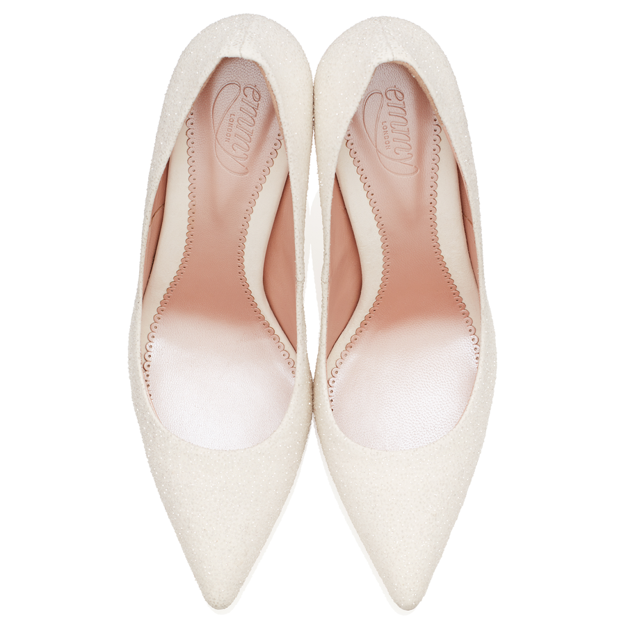 Elegant white pointed-toe pumps with a textured finish, featuring a sleek design and a smooth interior. The shoes are displayed from a top-down angle against a clean white background. image