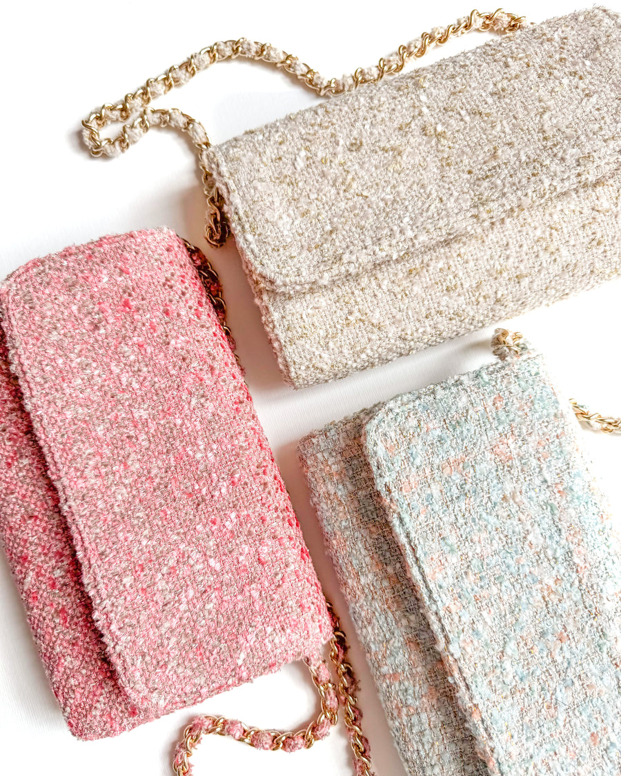 Three stylish tweed clutches are displayed on a white background. The clutches are in shades of pink, cream, and light blue, each featuring a gold chain strap. The image captures the bags from a top-down angle, showcasing their textured surfaces and elegant design. image