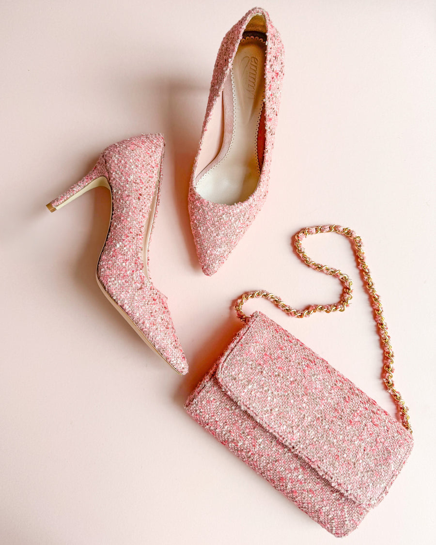 Pink glitter heels with a pointed toe design, featuring a stiletto heel. The heels are placed on a soft pink background alongside a matching pink glitter clutch bag. The angle of the image showcases the shoes from the side, highlighting their elegant silhouette. image